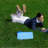 Una chica tumbada en el césped trabaja con su portátil