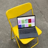 Un portátil abierto sobre una silla plegable amarilla